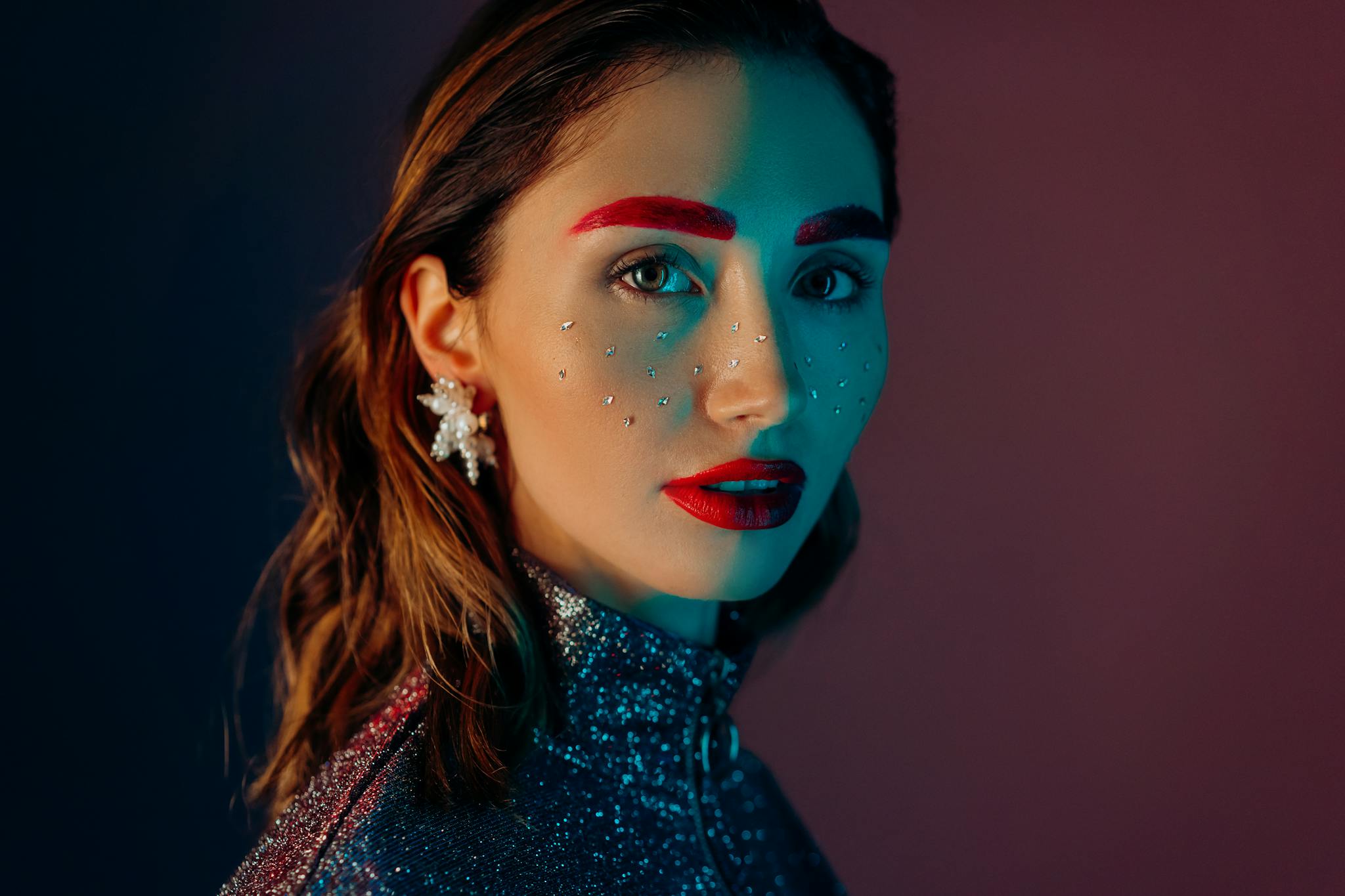 A striking portrait of a woman with vibrant makeup, glitter, and jewels, showcasing fashion and beauty creativity.