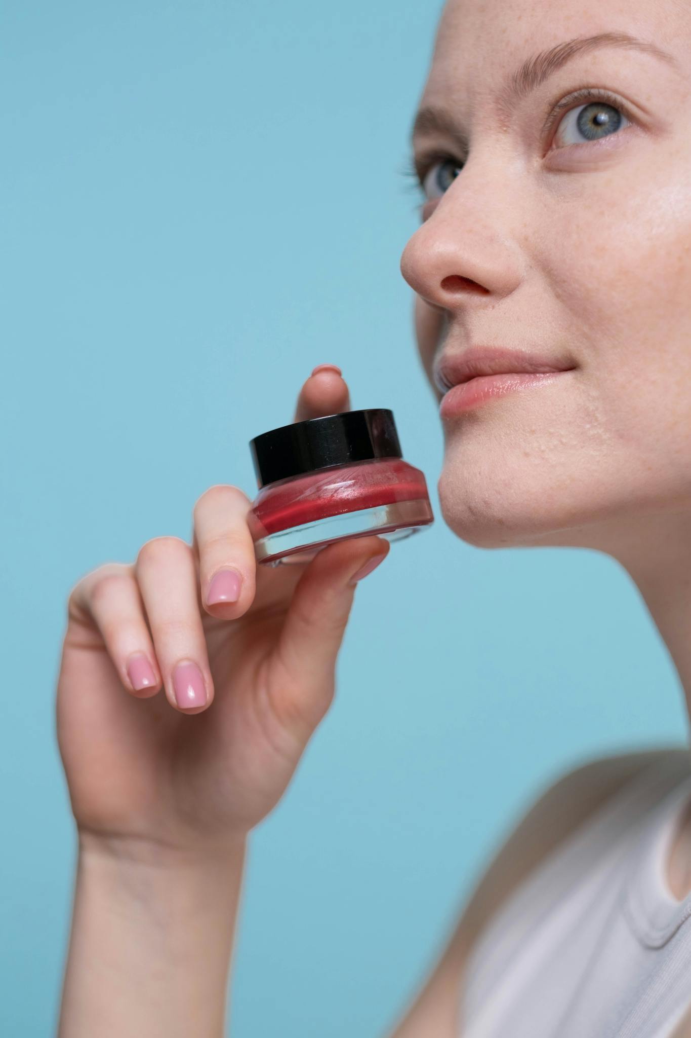 Woman holding cosmetic product against blue background, showcasing skincare and beauty theme.